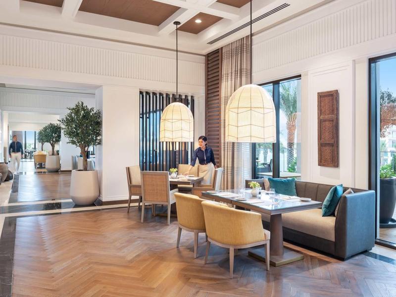 Moderner Wohnbereich mit braunem Holzboden, hohen Fenstern, Sesseln und Pflanzen am Fenster.