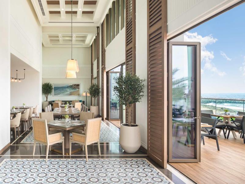 Moderner Balkon mit Holzboden, Pflanzen und Sitzbereich, offen zum Meer bei blauem Himmel.