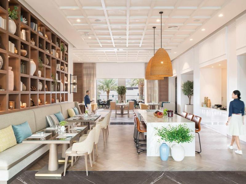 Helles Café mit Holzregalen, Sitzbank, Stühlen, Pflanzen und großen Fenstern, moderne Einrichtung.