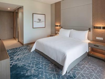 Moderner schlichter Schlafzimmer mit großem Bett, weißer Bettwäsche und blau-grauem Teppich.