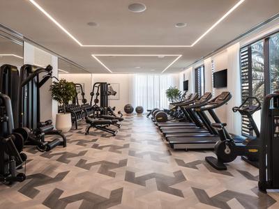 Moderner Fitnessraum mit Laufbändern, Kraftgeräten und großem Fenster mit Blick ins Freie.