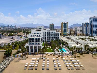 Modernes Hotel mit Pool und Liegestühlen am Sandstrand und Blick auf die Stadt