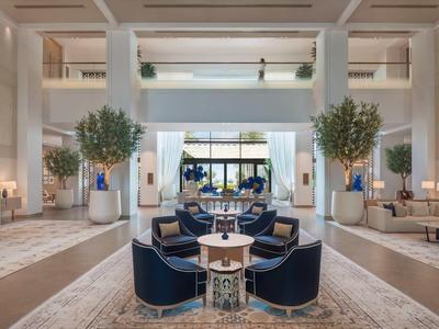 Großer, heller Hotel-Lobbybereich mit blauen Sesseln, Bäumen und moderner Beleuchtung.