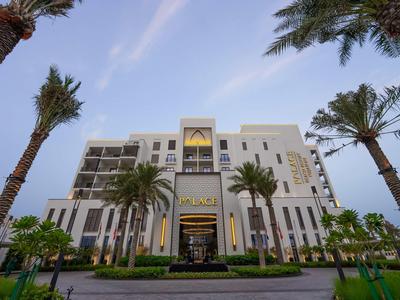 Modernes, weißes Hotelgebäude mit mehreren Stockwerken, umgeben von Palmen und blauem Himmel.