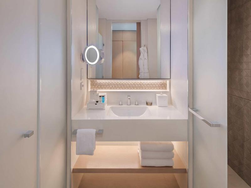 Moderner Hotelpool mit klar blauem Wasser, Palmen, Liegen und weißem Gebäude im Hintergrund.