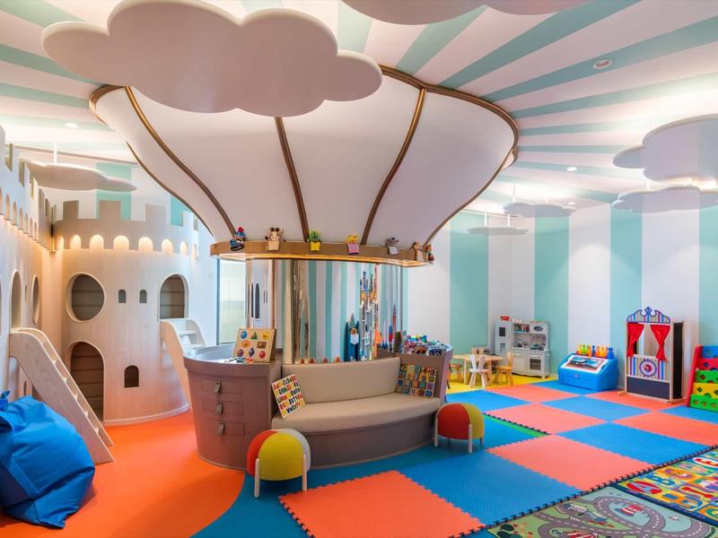 Bunter Kinderspielraum mit Heißluftballon-Sitzbereich, Wolken-Dekor und weichen Spielmatten.