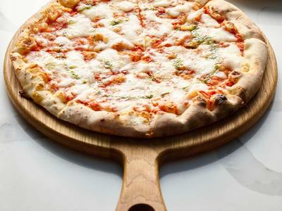 Runde Pizza mit Käse und Tomatensauce auf Holzbrett, weiße Teller und Serviette im Hintergrund.