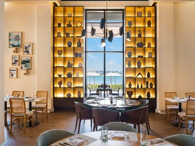 Elegantes Restaurant mit großen Fenstern, warmen Holzmöbeln und dekorativen Regalen mit Beleuchtung.