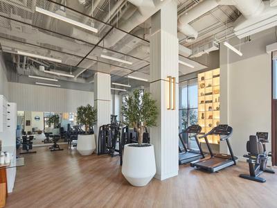 Moderner Fitnessraum mit Laufbändern, Fitnessgeräten und großen Fenstern in einem Hotel.