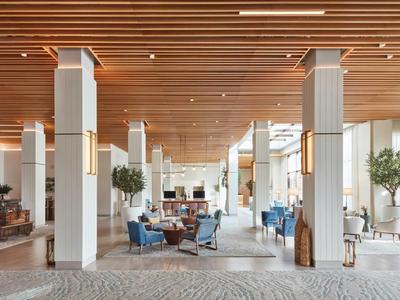 Heller, moderner Innenraum mit Holzdecke, weißen Säulen, blauem Mobiliar und vielen Pflanzen.