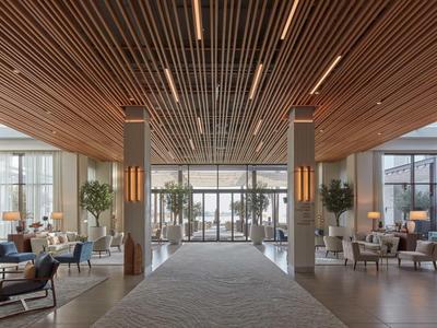 Heller Hotellobby mit Holzdecke, Sitzecken und großen Fenstern zur Außenterrasse.