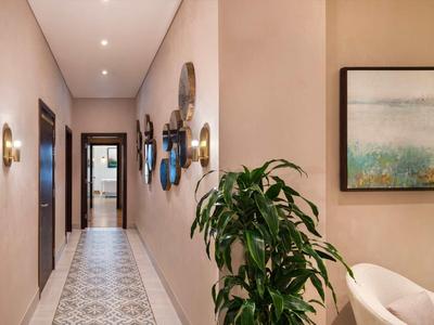 Heller Flur mit gemustertem Boden, Wandlampen, Pflanzen und mehreren Türen in neutralen Tönen.