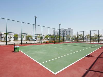 Ein Tenniscourt mit rotem und grünem Belag umgeben von einem Zaun und Gebäuden im Hintergrund.