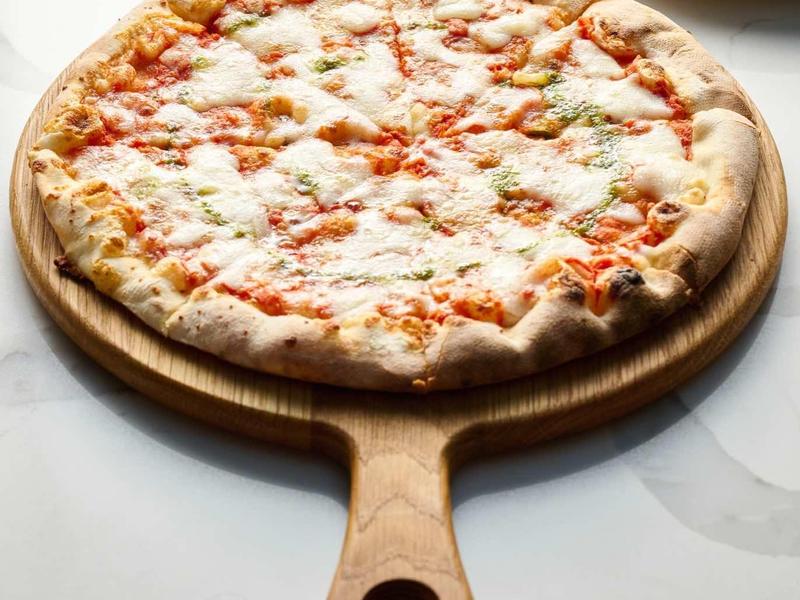 Runde Pizza mit Käse und Tomatensauce auf Holzbrett, weiße Teller und Serviette im Hintergrund.