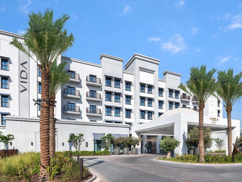 Weißes modernes Hotel mit mehreren Etagen, Palmen und blauen Himmel im Hintergrund.