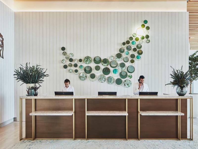 Moderner Empfangsbereich mit Holztheke, zwei Rezeptionisten und grüner Wanddekoration.