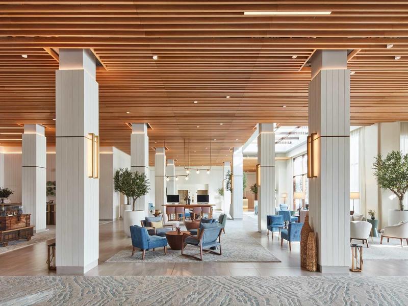 Heller, moderner Innenraum mit Holzdecke, weißen Säulen, blauem Mobiliar und vielen Pflanzen.