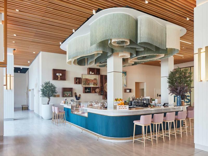 Moderner Gastraum mit rundem blauem Bar, rosa Hockern, Holzdecke und grünen Pflanzen.