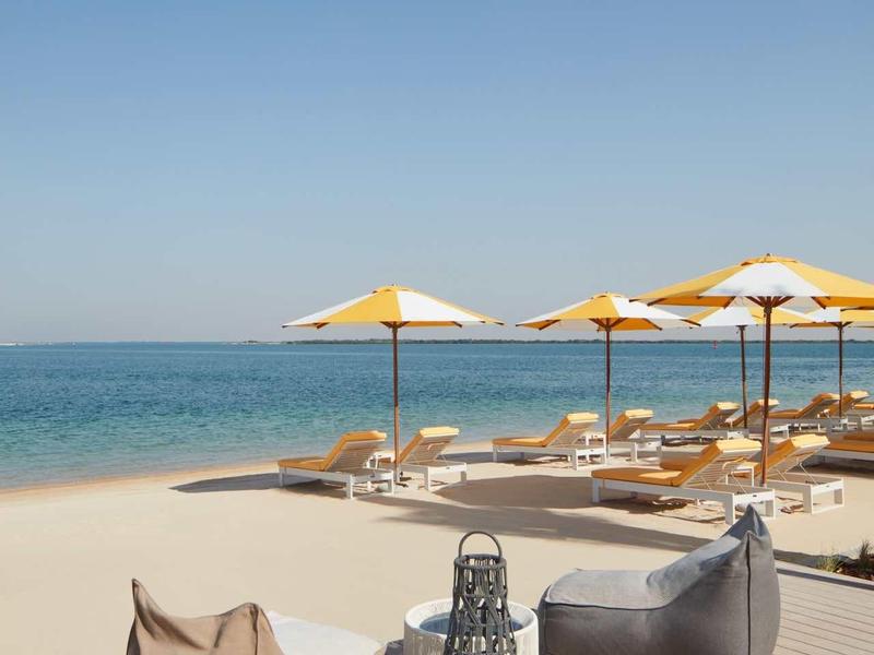 Strand mit Holzdeck, bunten Liegestühlen, Sonnenschirmen und klarem blauem Himmel am Meer.