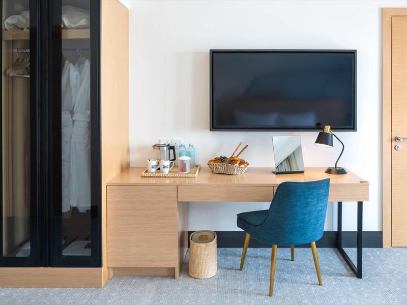 Moderner Arbeitsbereich mit Holzschreibtisch, blauem Stuhl, Fernseher und Schrank in hellem Raum.
