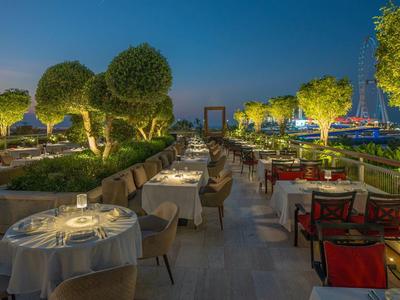 Illuminated outdoor restaurant terrace with set tables and tree decor at sunset.