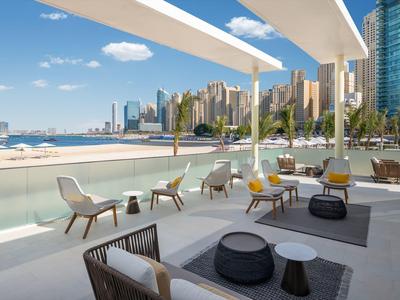 Modern terrace with chairs and tables by high-rise buildings near water