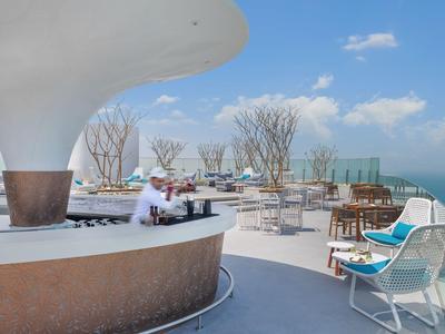 Terrasse sur le toit ouverte avec bar, sièges et vue sur la mer sous un ciel dégagé.