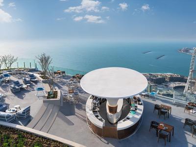 Terrasse avec espace de repos et vue sur la mer, reliée à un hôtel avec activités de loisirs.
