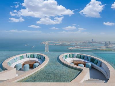 Piscine à débordement avec vue sur la ville et la mer sous un ciel bleu avec des nuages.