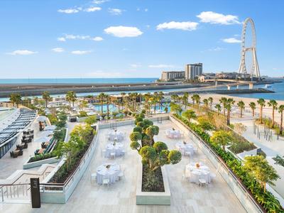 View of terrace with tables, palm trees and sea in the background with Ferris wheel under clear sky