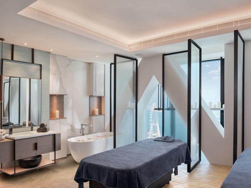 Modern spa with massage table, freestanding bathtub, and floor-to-ceiling windows overlooking the city