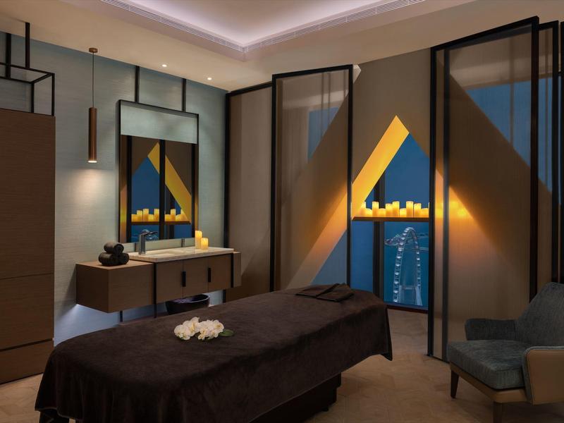 Modern spa treatment room with massage table, sink, and calming lighting.