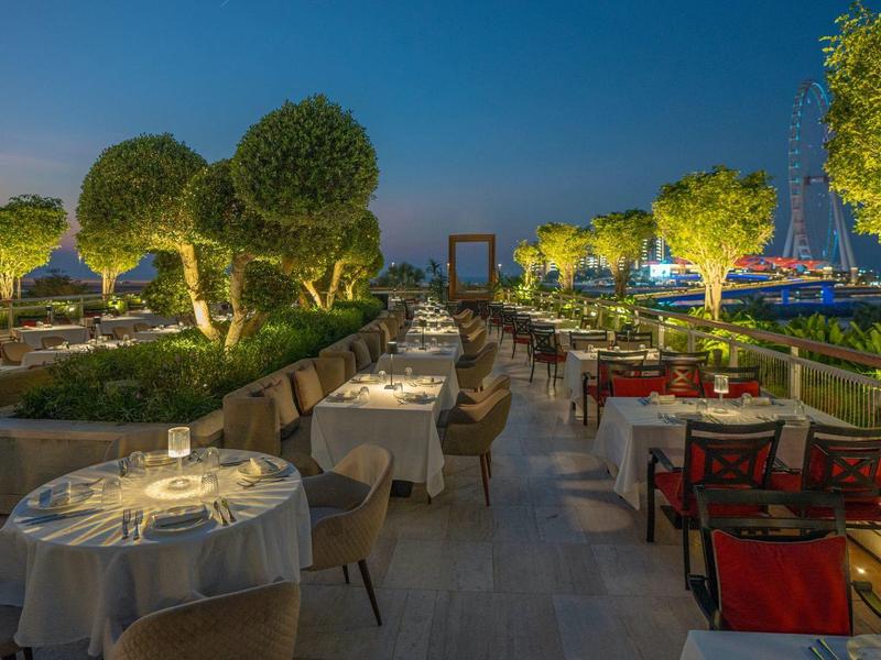 Illuminated outdoor restaurant terrace with set tables and tree decor at sunset.