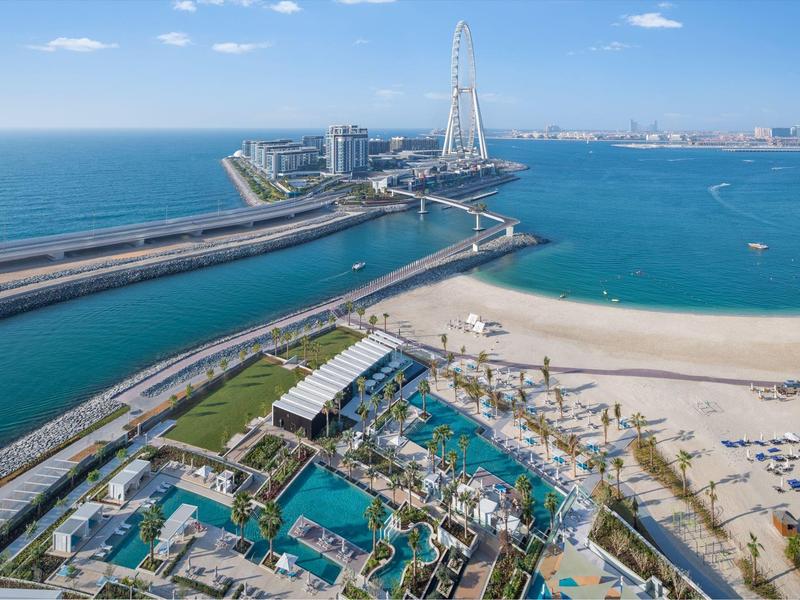 Overview of a beach and hotel resort with a large Ferris wheel and clear blue sea in the background.