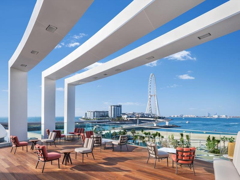 Terrace with chairs and tables, view of the sea and a Ferris wheel under clear sky