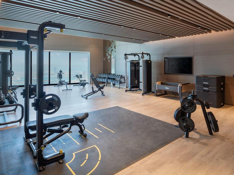 Modern gym with bench press, training equipment, and TV in a bright room.