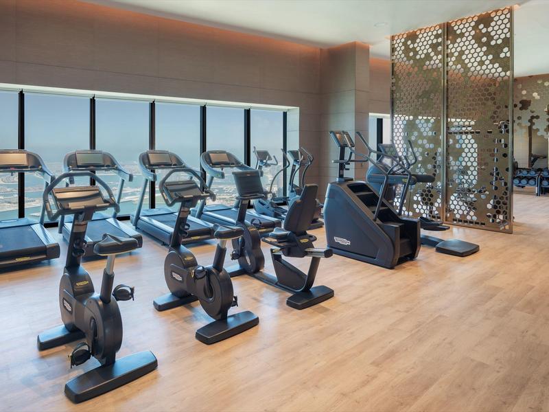 Modern gym with cardio machines in front of large windows and wooden flooring