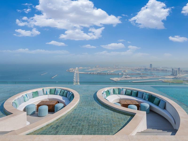 Luxury infinity pool lounge with round seating areas overlooking the sea and city.