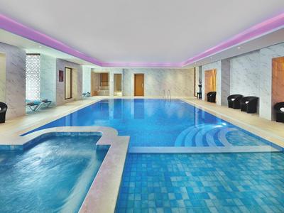 Innenpool mit angrenzendem Whirlpool, blauer Fliesenboden, moderne Deckenbeleuchtung und Sitzbereiche.