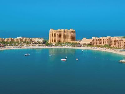 Bucht mit klarem blauem Wasser, umgeben von Sandstrand und mehreren großen Resorts.