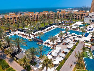 Luxusní hotelový komplex s několika bazény, lehátky a palmami za slunečného počasí.