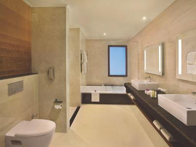 Modernes Bad mit weißem Waschbecken, Toilette, großer Badewanne und warmen beigen Wänden.