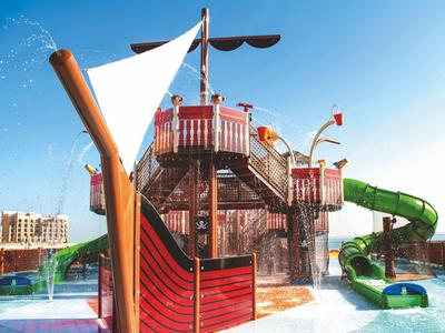 Wasserspielplatz mit einem großen Piratenschiff, Wasserrutschen und blauem Himmel im Hintergrund.