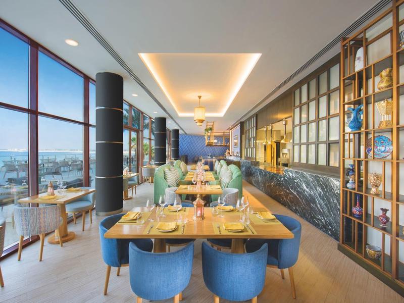 Modernes Restaurant mit großen Fenstern, blauen Stühlen und stilvoller Holz-Dekoration.