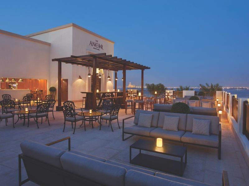 Dachterrasse mit Sitzbereich, Tischen und Stühlen bei Abenddämmerung, warm beleuchtet.