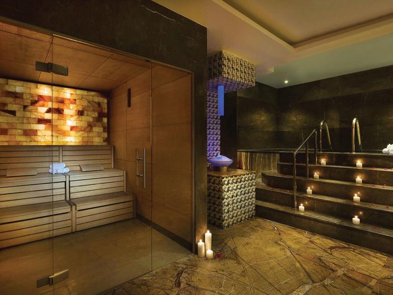 Moderne Sauna mit Holzbänken, indirekter Beleuchtung und Kerzen auf Natursteinboden.