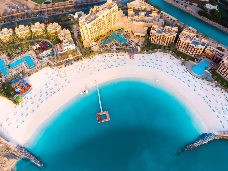 Luftaufnahme eines luxuriösen Resorts mit weißem Sandstrand und klarem blauem Wasser.