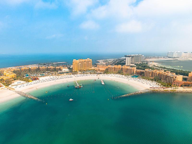 Luftaufnahme eines Strandes mit Hotels und klarem, blauem Wasser an der Küste.