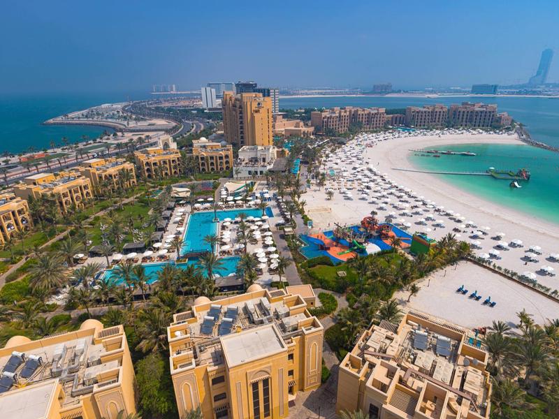 Luxuriöse Strand- und Poolanlage mit Hotels am türkisfarbenen Wasser bei sonnigem Wetter.