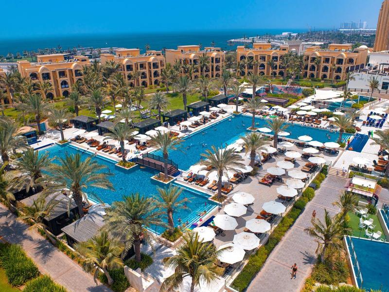 Luxuriöse Hotelanlage mit mehreren Pools, Liegestühlen und Palmen bei sonnigem Wetter.